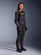 Alpinestars Woman Stella Dusk Leather Jacket, Black Diva Pink and White, worn by a female model with black motorcycle pants and boots, featuring a sleek leather construction with pink detailing and white branding.