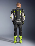 Alpinestars GP Tech V5 One Piece Leather Suit, Rear view, Black White and Yellow Fluo, featuring an aerodynamic speed hump with yellow star logo, white Alpinestars branding on sleeves and back, matching neon yellow racing boots, professional motorcycle track gear