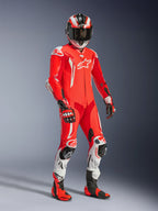 Motorcycle rider wearing the Alpinestars GP Tech V5 One Piece Leather Suit, Red Fluo and Bright Red with White accents, featuring matching helmet, gloves, and racing boots, professional track gear with perforated leather and protective sliders