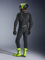 Rear view of a rider wearing the Alpinestars GP Force V2 1-Piece Leather Suit in Black, showing the aerodynamic speed hump and Tech-Air Ready branding, paired with a black and fluorescent yellow helmet and bright yellow racing boots.