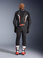 Rear view of a model wearing the Alpinestars GP Force V2 1-Piece Leather Suit in Black White Red Fluo, highlighting the aerodynamic speed hump and Tech-Air Ready branding, paired with white and red professional racing boots and black gloves.