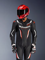 Motorcycle rider wearing Alpinestars GP Force V2 1-Piece Leather Suit in Black White Red Fluo, coordinated red racing helmet and gloves, features perforated leather panels and bold branding, high-performance racing gear