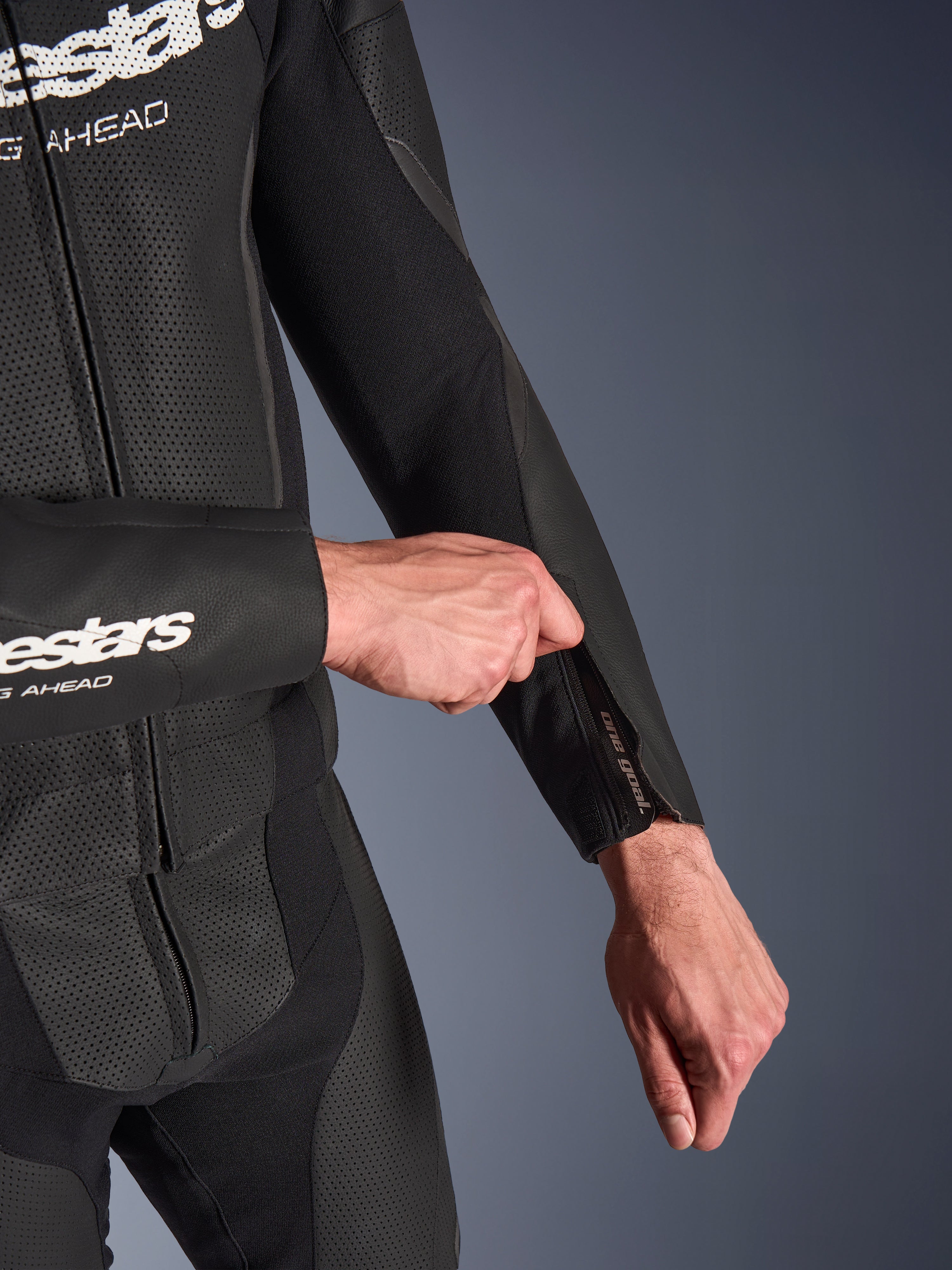 Alpinestars GP Force V2 2-Piece Leather Suit in Black, detail shot of the zippered forearm opening being adjusted, featuring perforated leather panels and stretch fabric construction.
