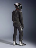 Alpinestars GP Force V2 2-Piece Leather Suit, Black, rear view of motorcycle rider wearing full racing gear, featuring aerodynamic speed hump, white branding, and perforated leather, paired with a carbon fiber helmet and black and white racing boots
