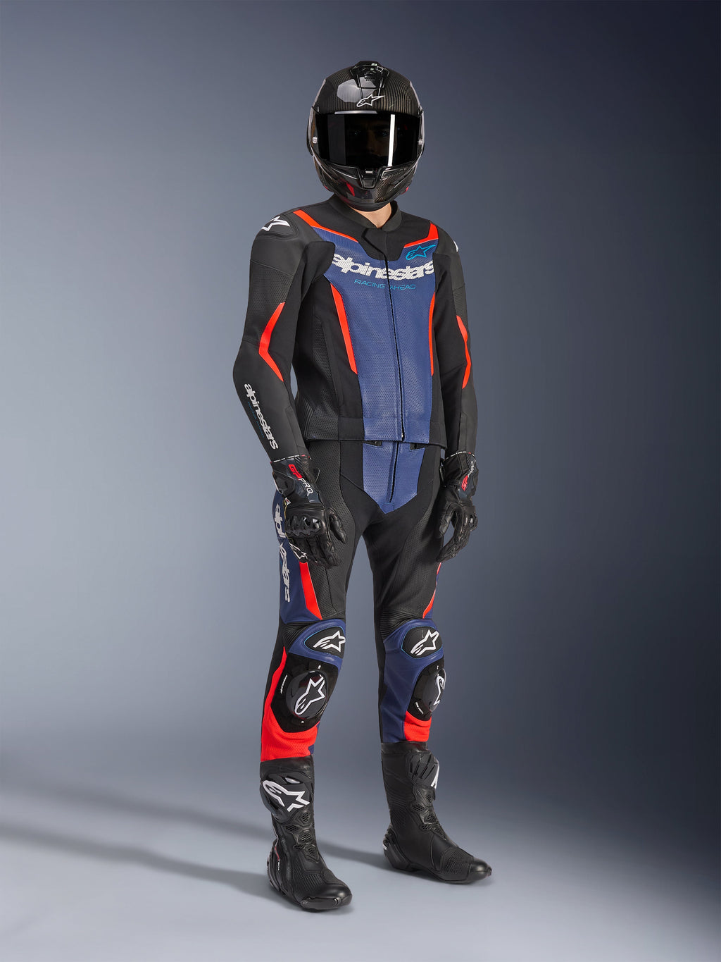 Alpinestars GP Force V2 Leather Suit - 2Piece in Black, Blue, and Red Fluo, worn with a carbon fiber helmet, black racing gloves, and boots, featuring perforated leather panels and white Alpinestars logo, professional sport riding gear.