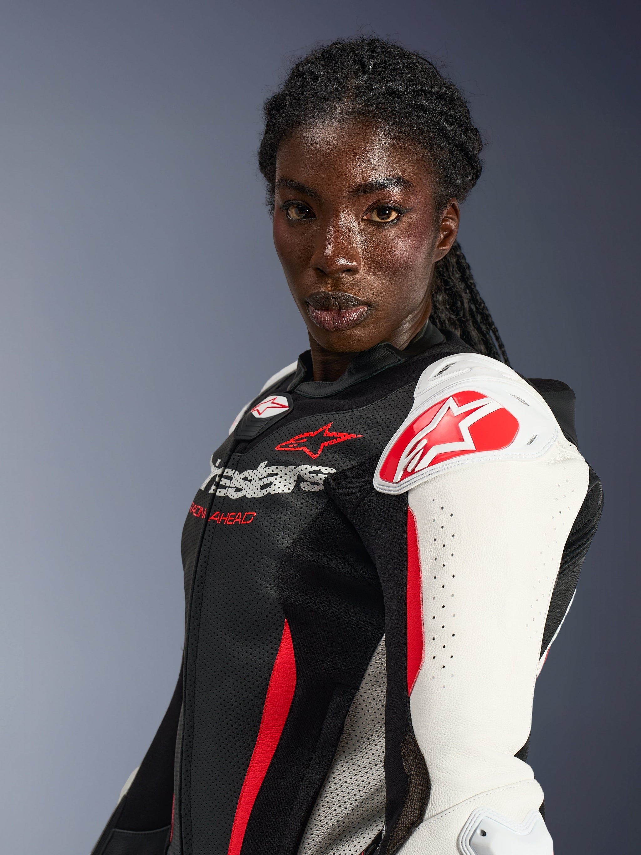 Female rider wearing Alpinestars Stella GP-R7 2-Piece Leather Suit, Black White and Red Fluo, featuring white shoulder protectors with red star logo, perforated leather chest, and professional racing-inspired design