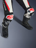 Alpinestars Woman Stella GP-R7 2-Piece Leather Suit, Black White and Red Fluo, close-up of legs and knees featuring red and white GP DFS RR sliders, perforated leather construction with accordion stretch panels, worn with black performance racing boots