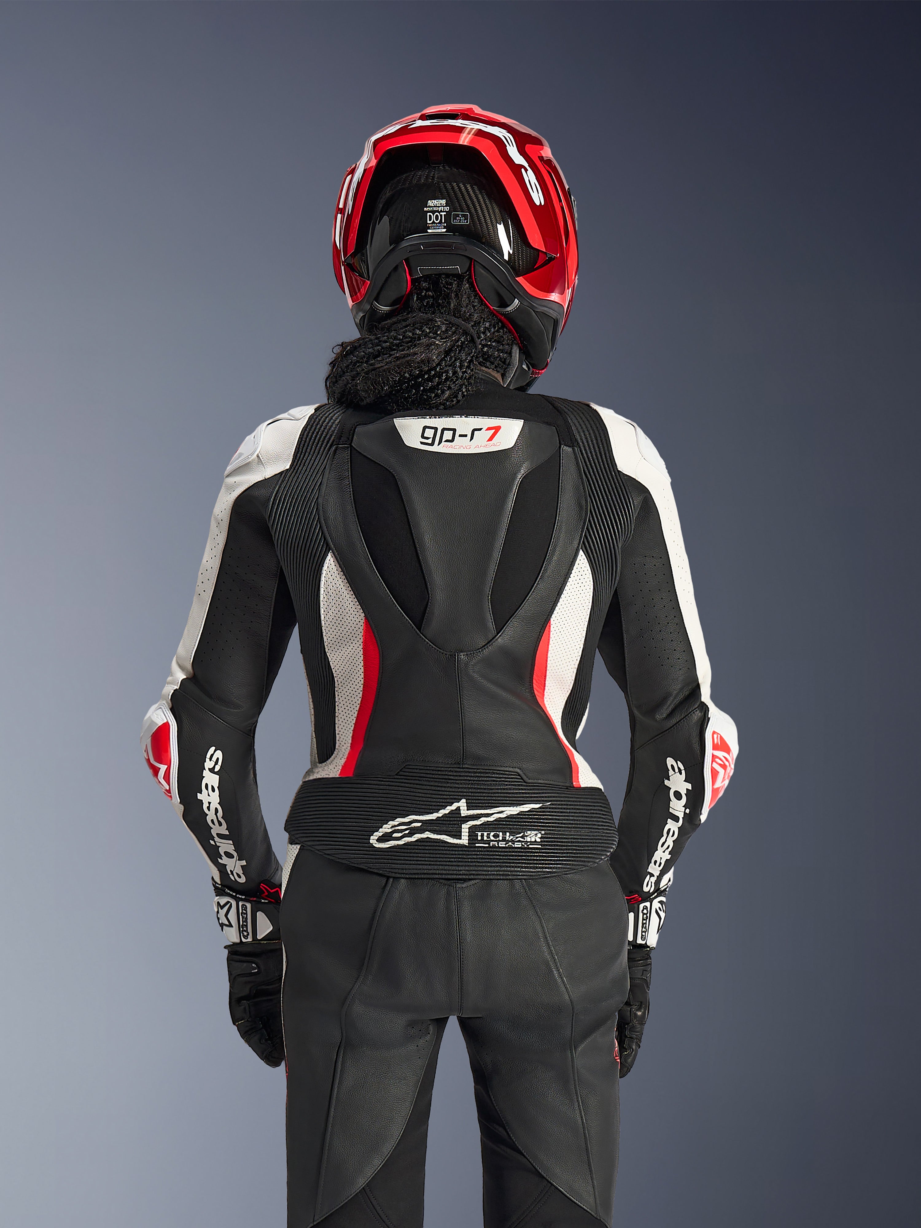 Alpinestars Woman Stella GP-R7 2-Piece Leather Suit, Black White and Red Fluo, back view of a rider wearing a red helmet and black gloves, featuring an aerodynamic hump with gp-r7 branding and Tech-Air Ready logo on the lower back.