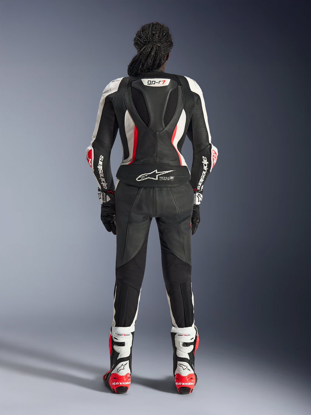 Rear view of the Alpinestars Stella GP-R7 2-Piece Leather Suit, Black White and Red Fluo, featuring an aerodynamic hump with GP-R7 branding and Tech-Air Ready logo, worn with matching racing boots and gloves, professional motorcycle gear for women