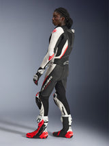 Woman wearing Alpinestars Stella GP-R7 2-Piece Leather Suit, Black White and Red Fluo, side profile showing aerodynamic back hump and knee sliders, paired with matching Alpinestars racing gloves and boots, professional motorcycle track gear