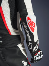 Close-up of the Alpinestars Woman Stella GP-R7 2-Piece Leather Suit, Black White and Red Fluo, featuring the GP DFS RR elbow slider with a red star logo, white Alpinestars wordmark on the forearm, and detailed perforated leather and accordion stretch panels.