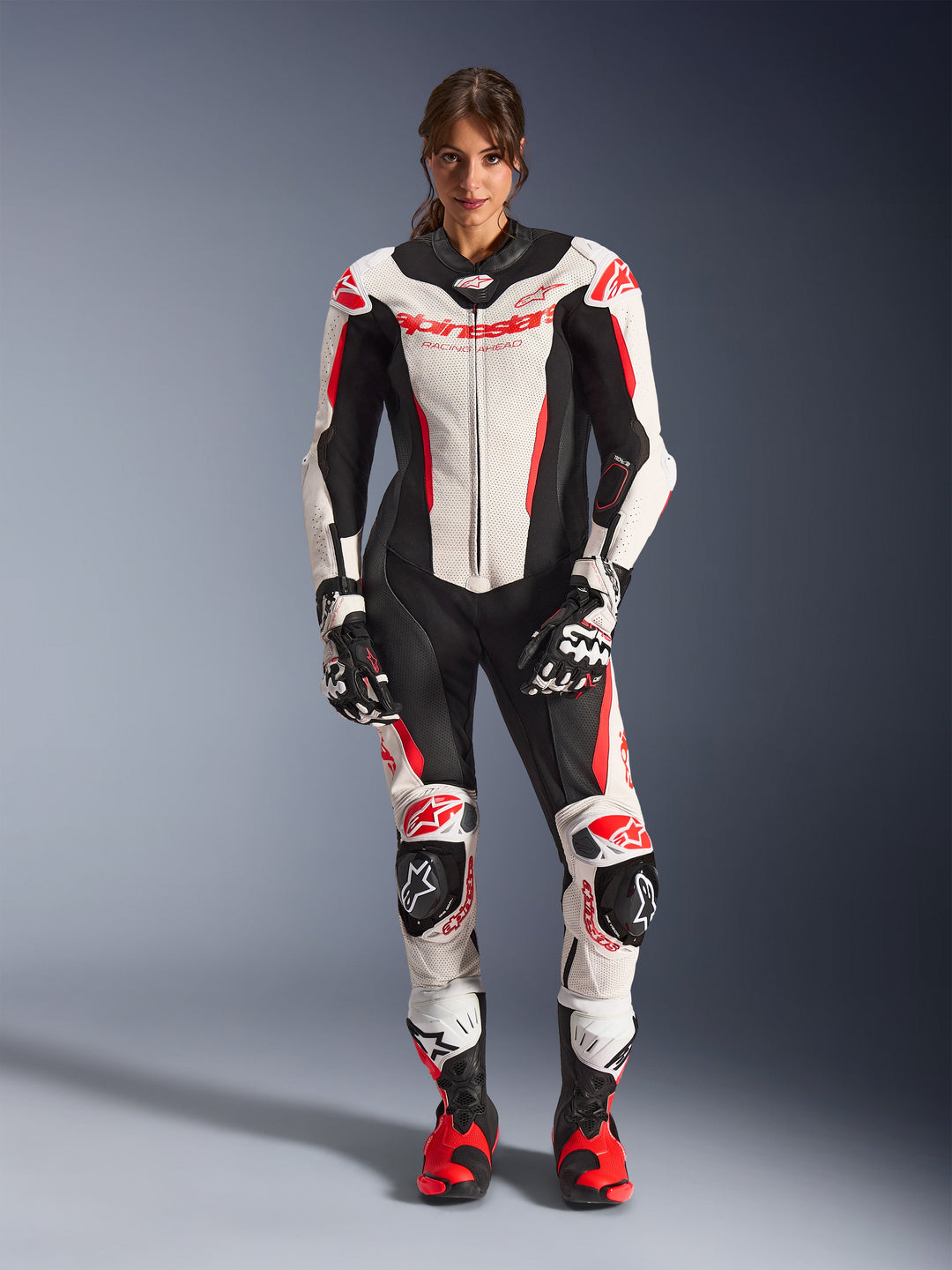 Female rider wearing Alpinestars Stella GP-R7 1-Piece Leather Suit, White Black and Red Fluo, race-ready motorcycle gear with perforated leather panels and integrated armor, paired with matching gloves and racing boots