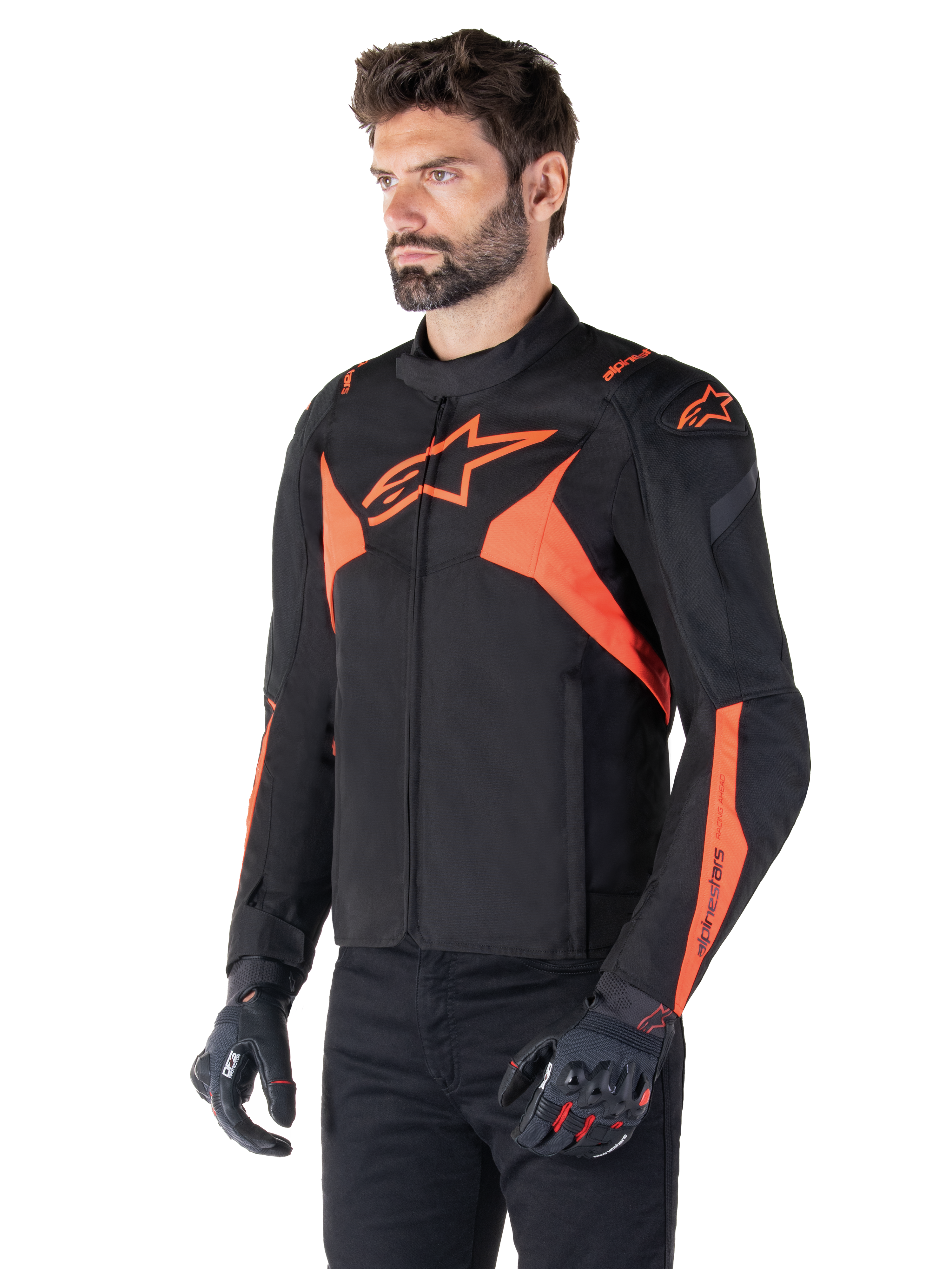 Alpinestars T-Jaws V4 Waterproof Jacket, Black and Red Fluo, sport motorcycle jacket worn by a male model, featuring prominent orange star logos on the chest and shoulders, paired with black gloves and pants