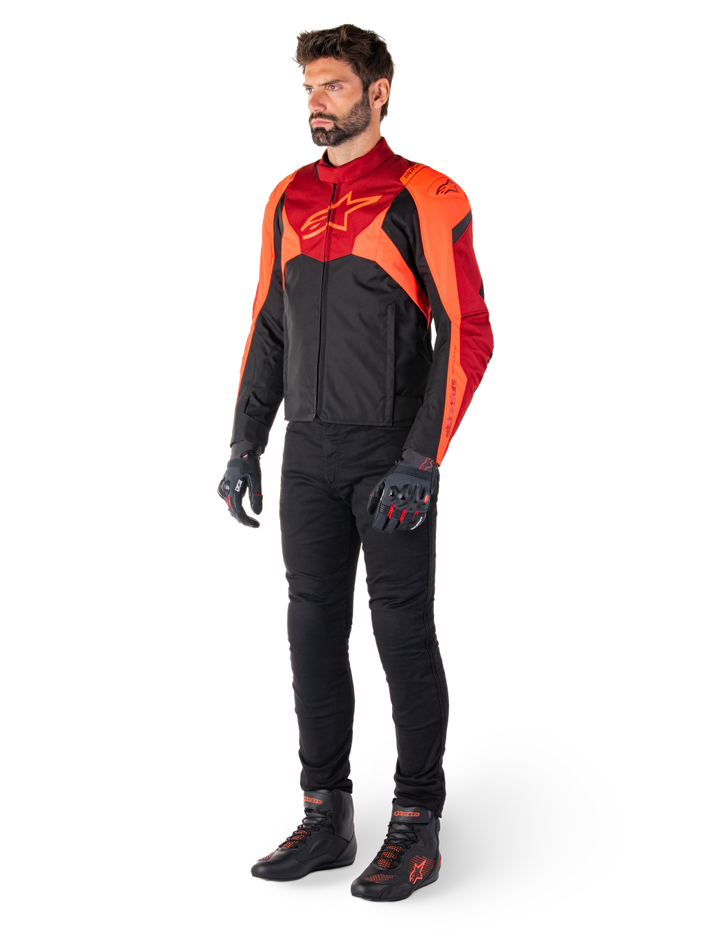 Male rider wearing the Alpinestars T-Jaws V4 Waterproof Jacket in Black Red Fluo Dark Red, paired with black motorcycle pants, gloves, and riding boots, featuring a sport-fit textile design with bold chest branding and an aggressive silhouette.