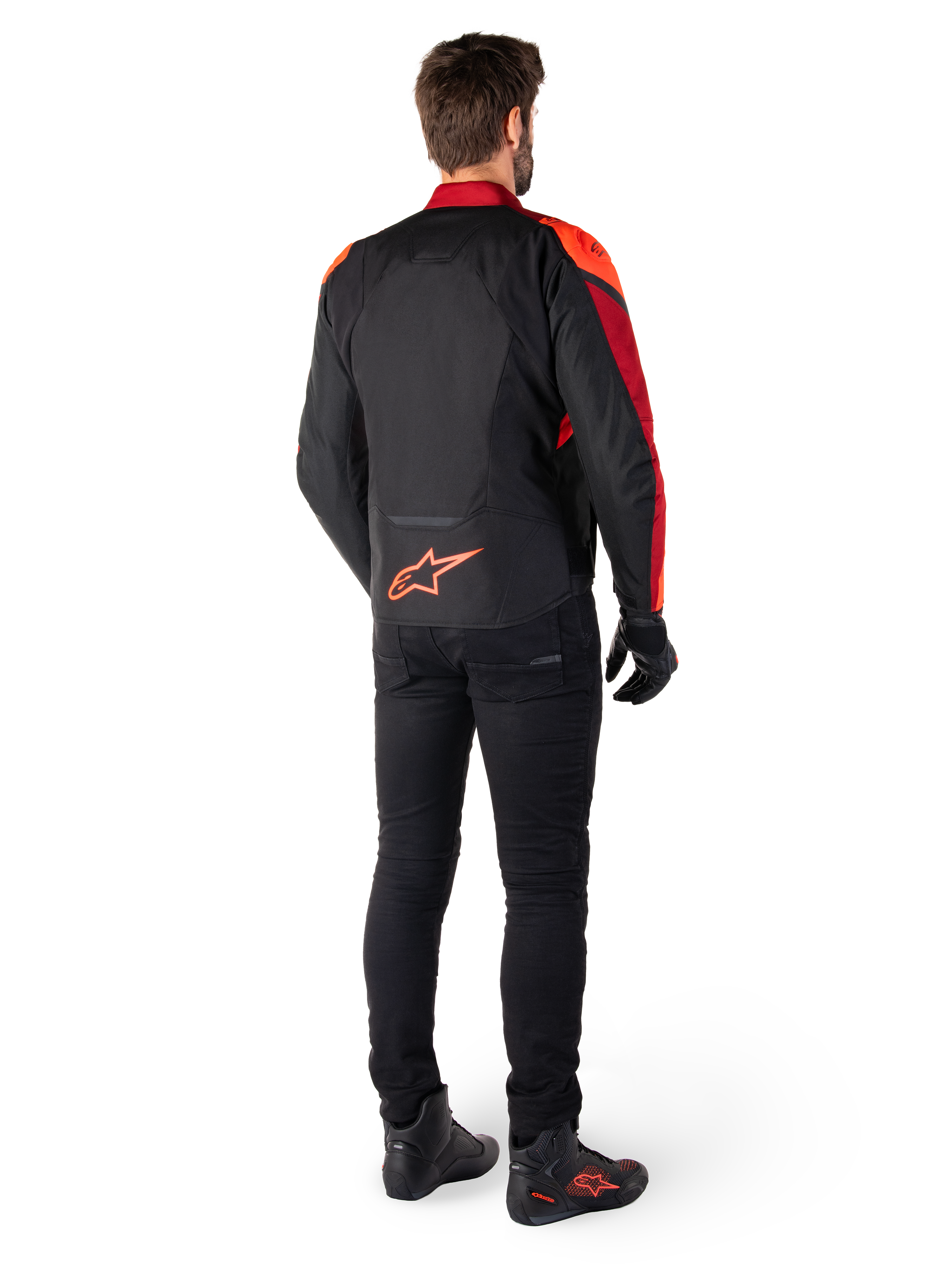 Alpinestars T-Jaws V4 Waterproof Jacket in Black Red Fluo Dark Red, rear view of a rider wearing the textile jacket with black pants and riding boots, featuring a bold red Alpinestars logo on the lower back.