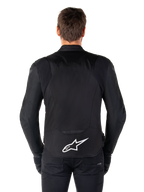 Alpinestars T-Jaws V4 Waterproof Jacket, Black motorcycle jacket seen from the back, featuring a white Alpinestars logo on the lower back, extended rear for coverage, worn by model with black pants and gloves, sleek sport textile design