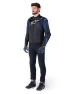 Alpinestars T-Jaws V4 Waterproof Jacket in Black, Dark Blue, and Blithe Blue, worn by a model with black motorcycle pants and riding boots, featuring white Alpinestars logo on chest and blue shoulder accents, sport-fit riding gear.