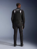 Alpinestars T-SP 1 V2 Waterproof Jacket, Black and White, rear view of a rider wearing the jacket with matching black motorcycle pants and boots, featuring a white A-star logo on the upper back and reflective shoulder panels, sport textile riding gear