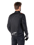 Alpinestars T-SPS V2 Waterproof Jacket, Black White Red Fluo, rear view, featuring white Alpinestars logo on the lower back and red accents on the shoulders, worn with black riding gloves and pants, sport-style textile motorcycle jacket.