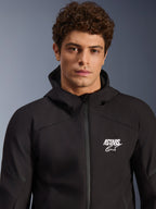 Male model wearing Alpinestars Aeroshell Waterproof Jacket, black textile softshell hoodie, white ASTARS logo on chest, waterproof front zipper, modern studio portrait for motorcycle road gear.