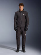 Male model wearing Alpinestars Aeroshell Waterproof Jacket in Black, paired with matching black technical pants and riding gloves, featuring a hooded softshell design with white logo accents, modern motorsport-inspired outfit for road riding