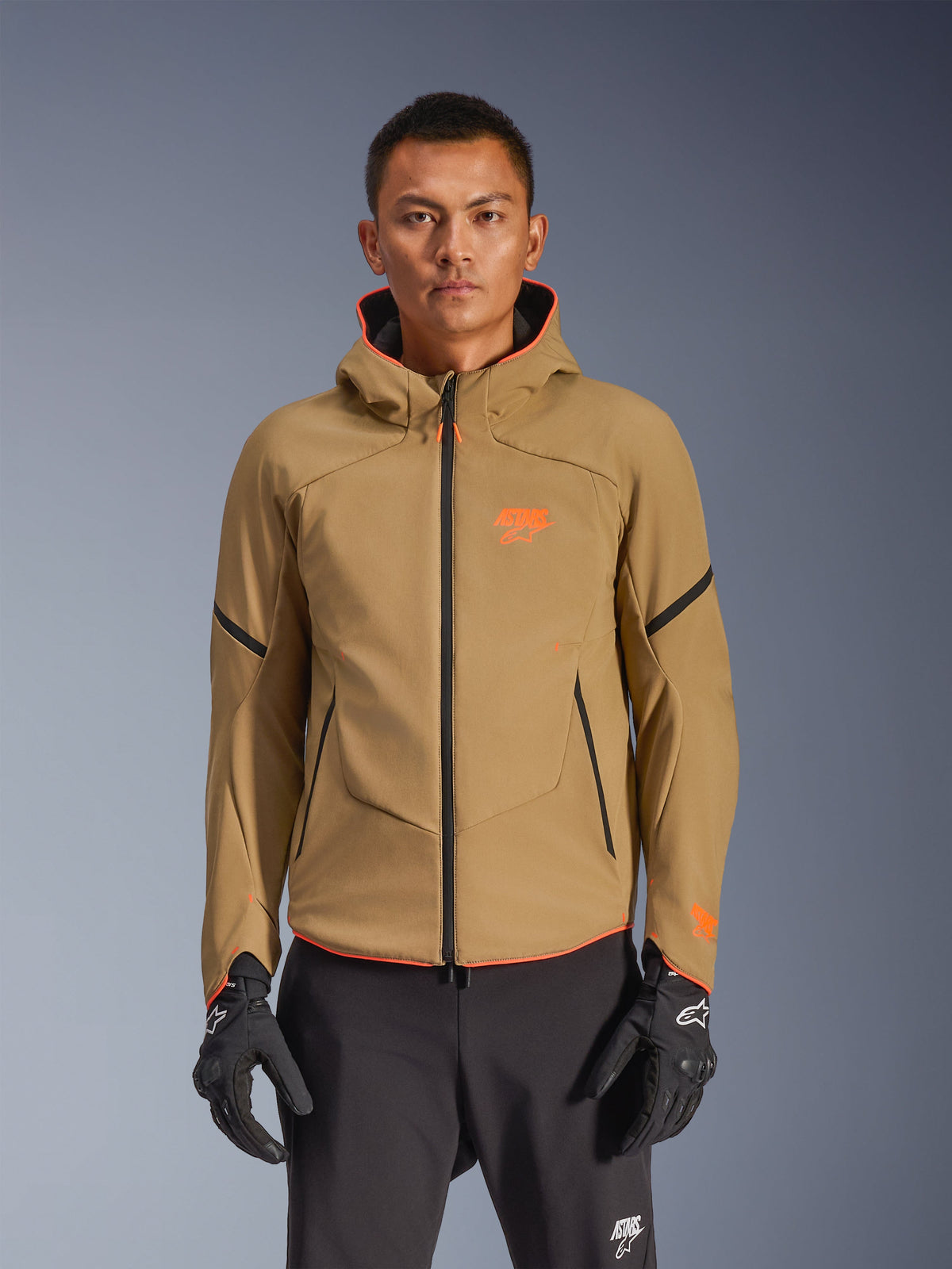 Alpinestars Aeroshell Waterproof Jacket, Dark Khaki hooded motorcycle jacket with orange logos and black zippers, black accent lines on sleeves, shown with black gloves and pants
