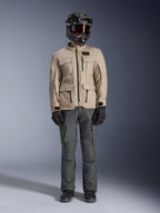 Alpinestars Borrego Drystar® Jacket in Warm Gray, adventure motorcycle jacket with four front cargo pockets, paired with dark gray riding pants, black off-road helmet, and black gloves, featuring a rugged waxed-canvas look