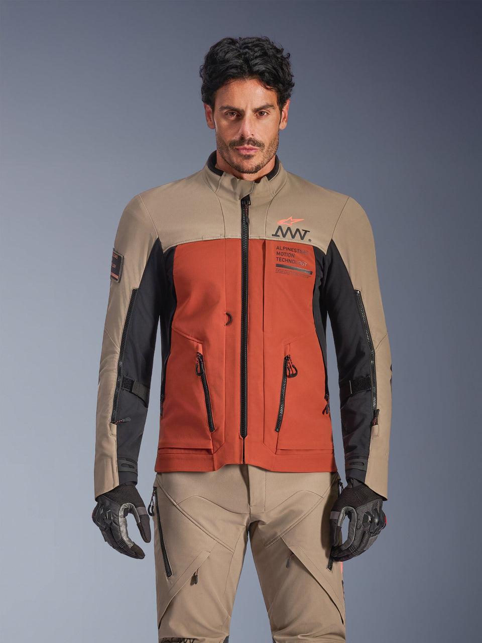 Alpinestars AMT-8 Stretch Drystar® XF Jacket, Walnut Rust Black adventure touring jacket, worn by male model with matching pants and gloves, featuring a tri-color tan, rust, and black design with AMT branding on the chest, active touring fit for motorcycle riding