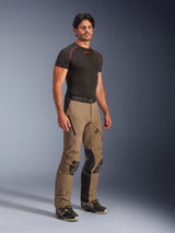 Alpinestars AMT-8 Stretch Drystar® XF Pants in Walnut Black, adventure touring motorcycle pants worn by a model with a black base-layer tee, featuring stretch material, zippered thigh vents, and protective knee panels.