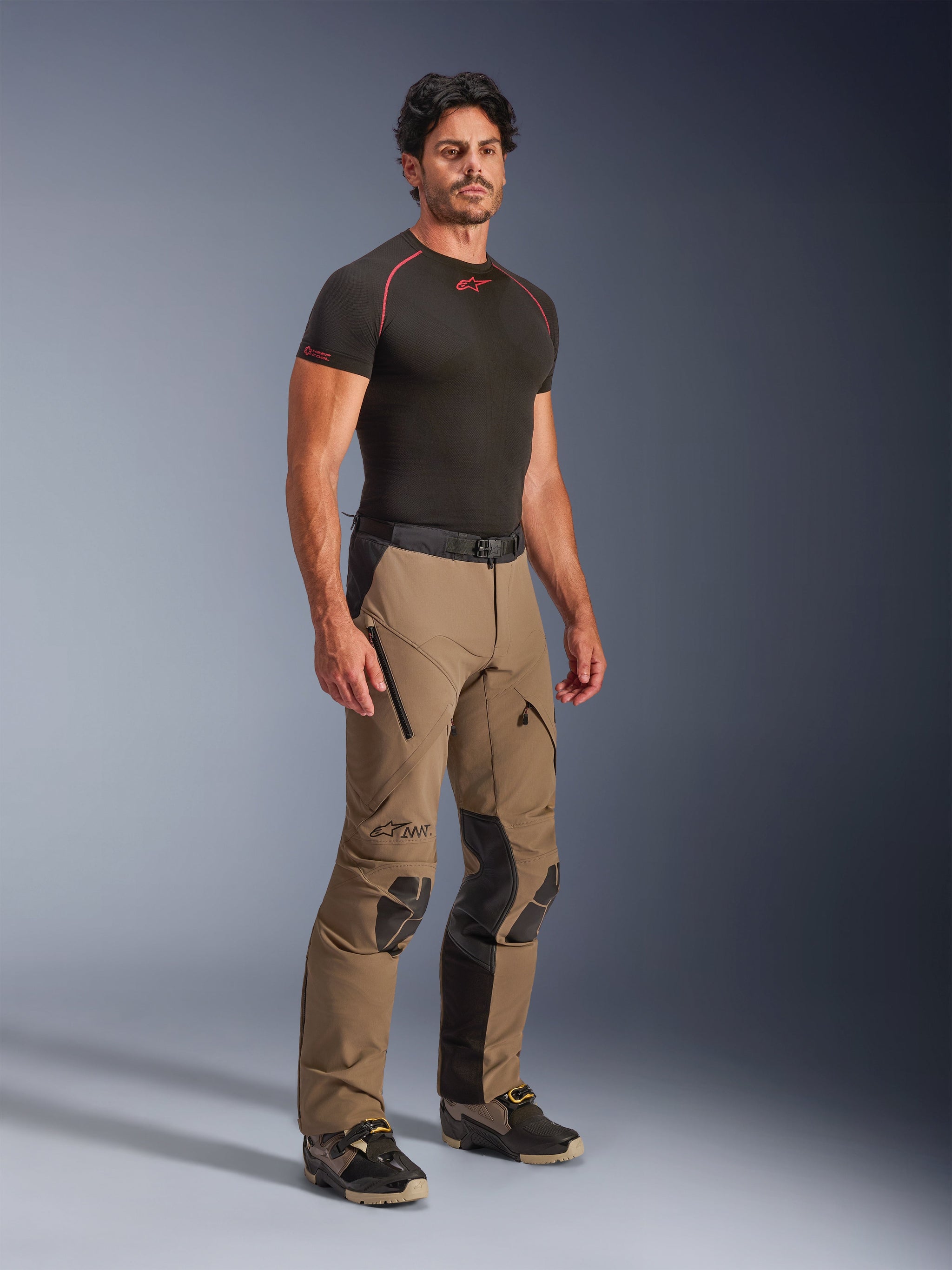 Alpinestars AMT-8 Stretch Drystar® XF Pants in Walnut Black, adventure touring motorcycle pants worn by a model with a black base-layer tee, featuring stretch material, zippered thigh vents, and protective knee panels.