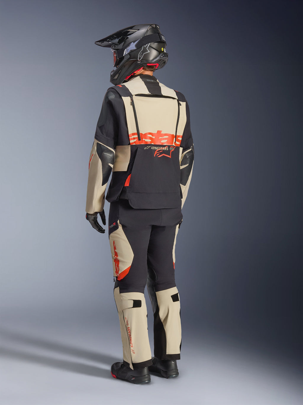 Alpinestars Halo Pro Drystar® XF Laminated Jacket, Mastic Black, rear view of a rider wearing the full adventure motorcycle suit with matching pants, black adventure helmet, and boots, featuring a bold red Alpinestars logo across the back.