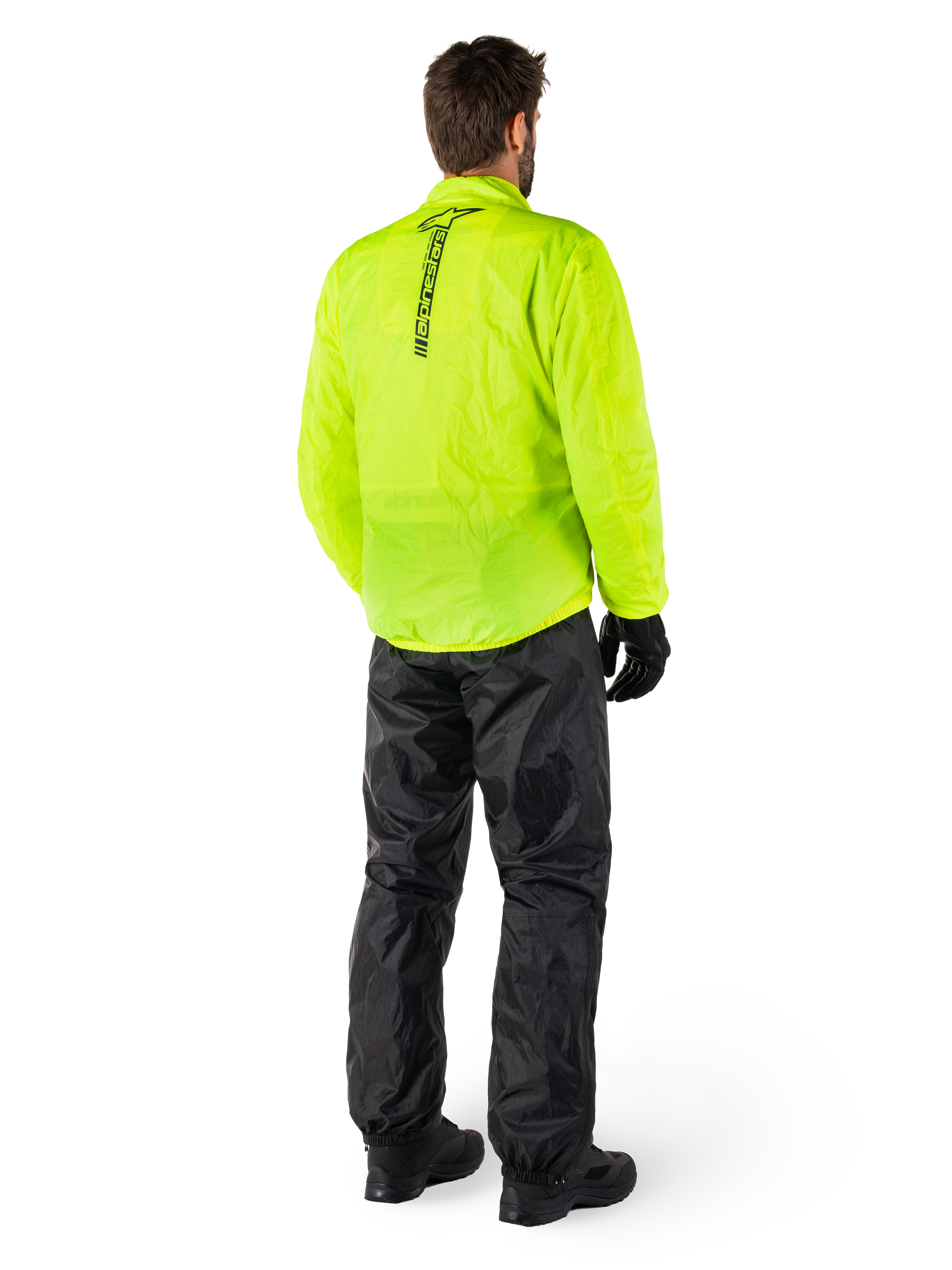 Person from the back wearing Alpinestars Hurricane Rain V2 Jacket in Yellow Fluo and Hurricane Rain V2 Pant in Black, vertical logo on jacket back, waterproof motorcycle rain gear with black gloves and boots