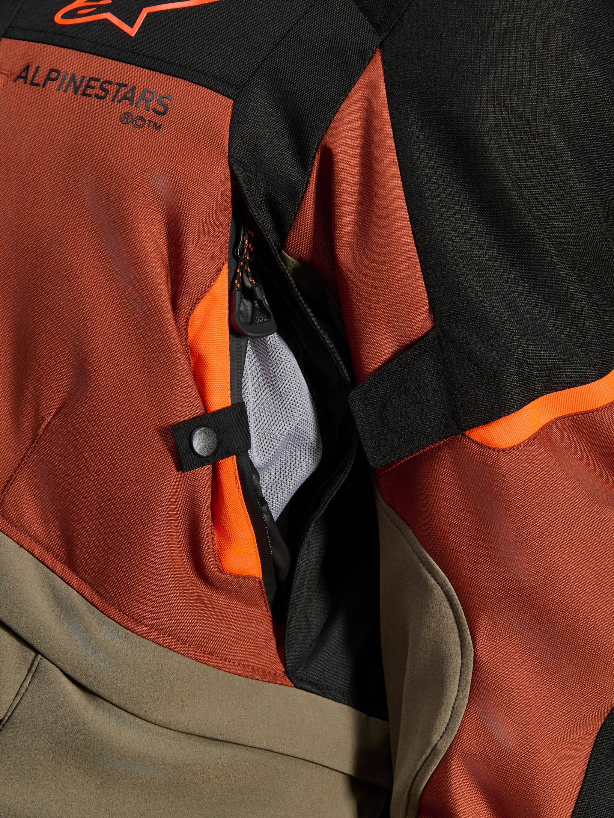 Alpinestars Andes V4 Drystar® Jacket, Walnut Rust Black, close-up of direct ventilation vent with mesh lining, durable textile material with orange accents, snap button and Alpinestars logo detail