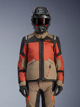 Alpinestars Andes V4 Drystar® Jacket, Adventure Motorcycle Jacket, Walnut Rust Black, worn with a matching helmet and gloves, featuring a technical multi-panel design in tan, reddish-orange, and black with visible orange branding and waterproof zippers.
