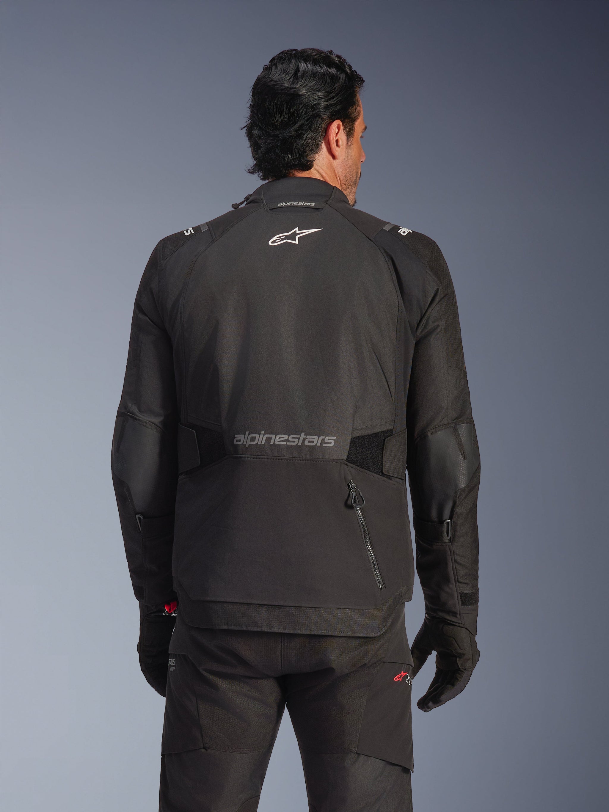Alpinestars Andes V4 Drystar® Jacket, Black, rear view on a model, textile adventure jacket with reflective logos and a zippered back pocket, styled with matching black pants and gloves