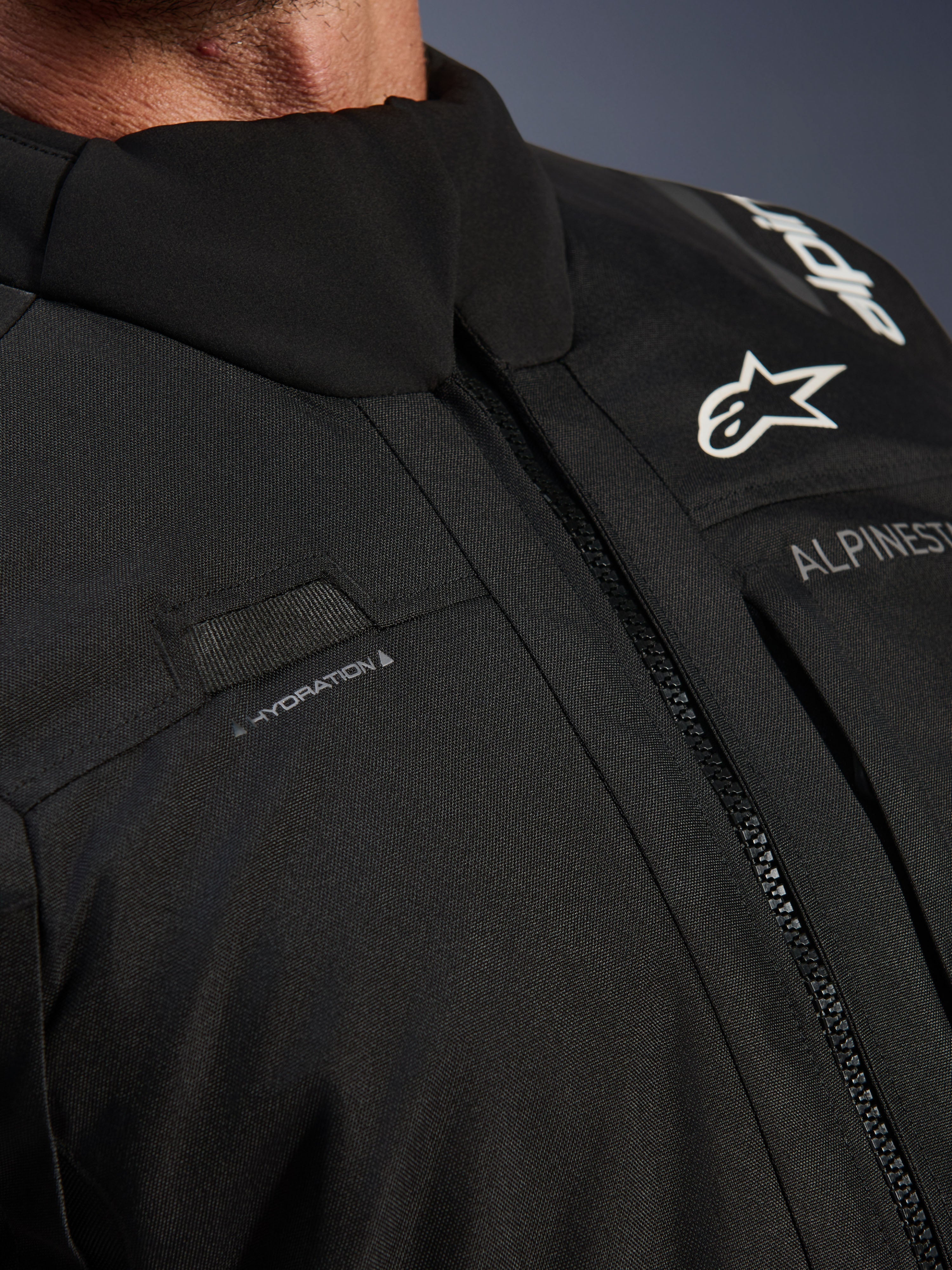 Alpinestars Andes V4 Drystar® Jacket, Black, close-up of chest detail featuring hydration hose loop, waterproof VISLON® front zipper, and Alpinestars logo on durable textile material
