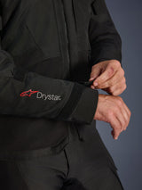 Alpinestars Andes V4 Drystar® Jacket, Black textile motorcycle jacket, close-up of the sleeve featuring red Alpinestars and white Drystar® branding, rider adjusting the velcro wrist strap for a secure fit, adventure riding functional detail