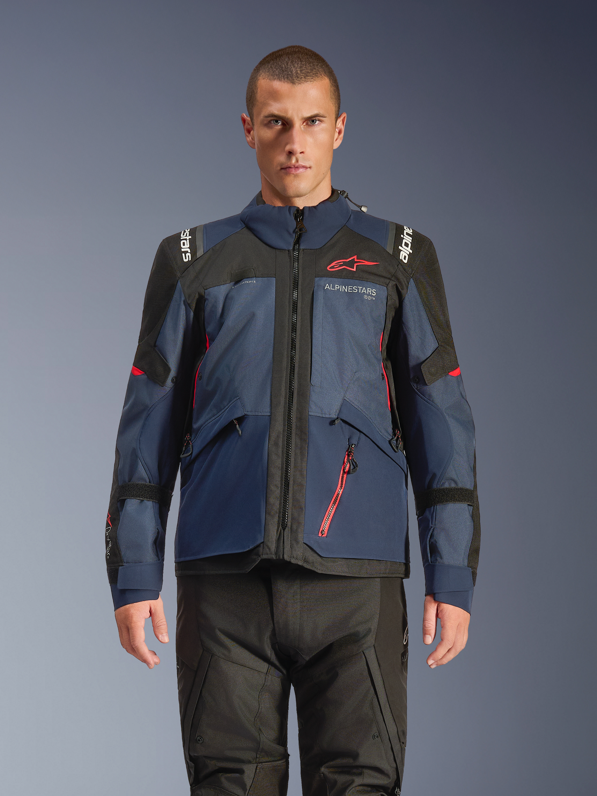 Alpinestars Andes V4 Drystar® Jacket, Adventure Motorcycle Jacket, Night Navy and Mood Indigo with Black panels, worn by model with black riding pants, red Alpinestars logo on chest and red zipper detail, durable textile construction for all-weather touring.