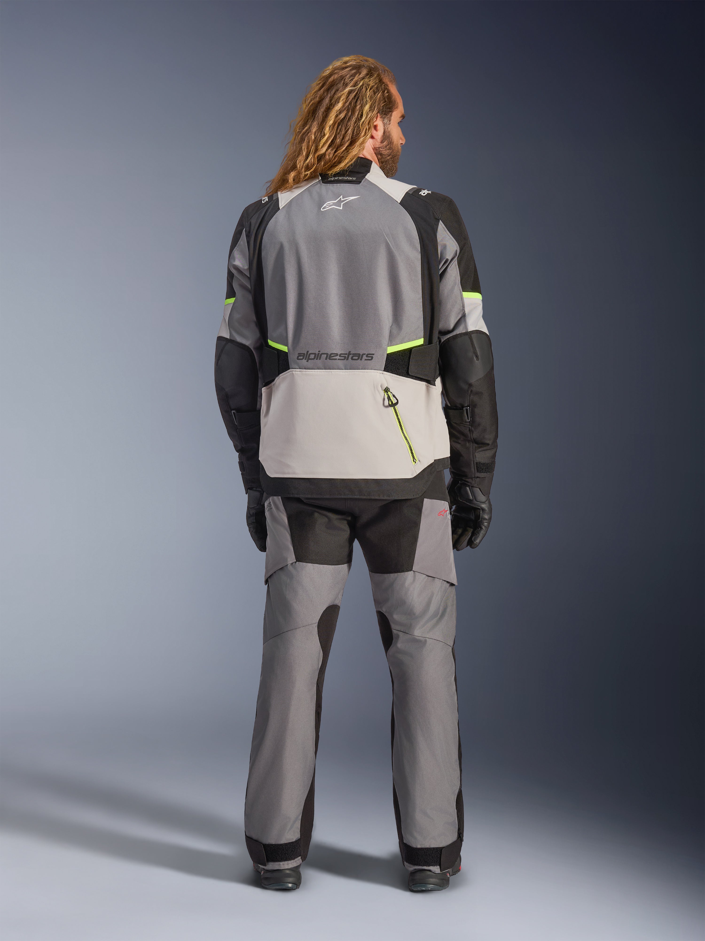 Alpinestars Andes V4 Drystar® Jacket, Adventure Motorcycle Jacket, Dark Gray and Ice Gray with Black and Yellow Fluo accents, rear view worn with matching pants and black gloves, featuring a large back pocket with yellow zipper and reinforced shoulder and elbow panels