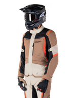 Alpinestars ST-1 Waterproof Jacket, Adventure Touring Jacket, Dark Khaki Sand Black and Red Fluo, worn by a rider with a black motocross helmet and goggles, featuring a multi-panel design with cargo pockets and Alpinestars branding on the chest
