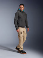 Male model wearing Alpinestars Moblast Waterproof Jacket in Black, urban motorcycle hoodie with teal-lined hood, paired with khaki cargo pants and black sneakers, modern minimalist design with technical stretch fabric for all-weather commuting