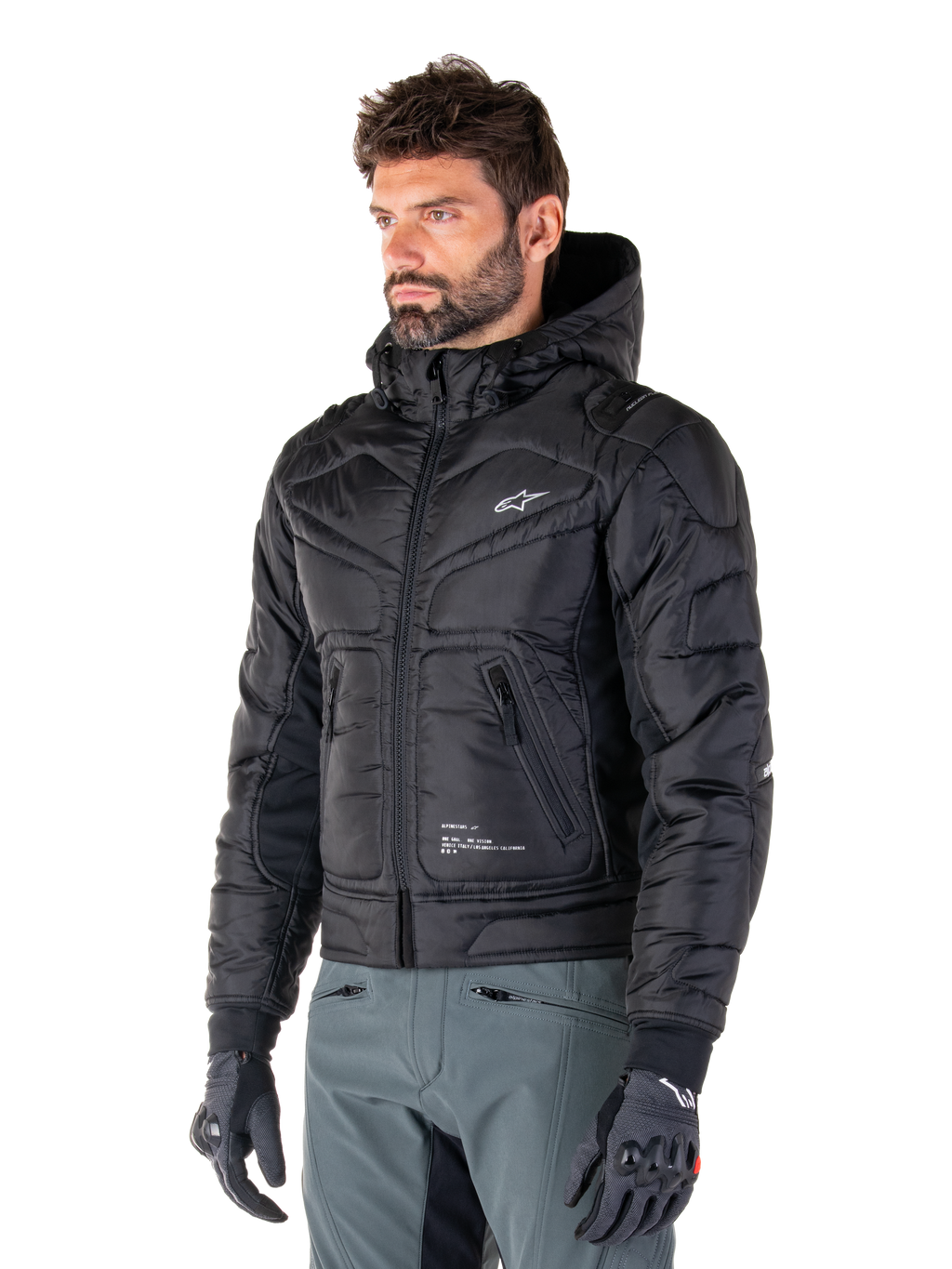 Alpinestars Mohobbs Waterproof Jacket, Black, quilted padded bomber design with a hood, worn by a man with grey riding pants and black gloves, urban streetwear-inspired motorcycle apparel featuring a small white logo on the chest.