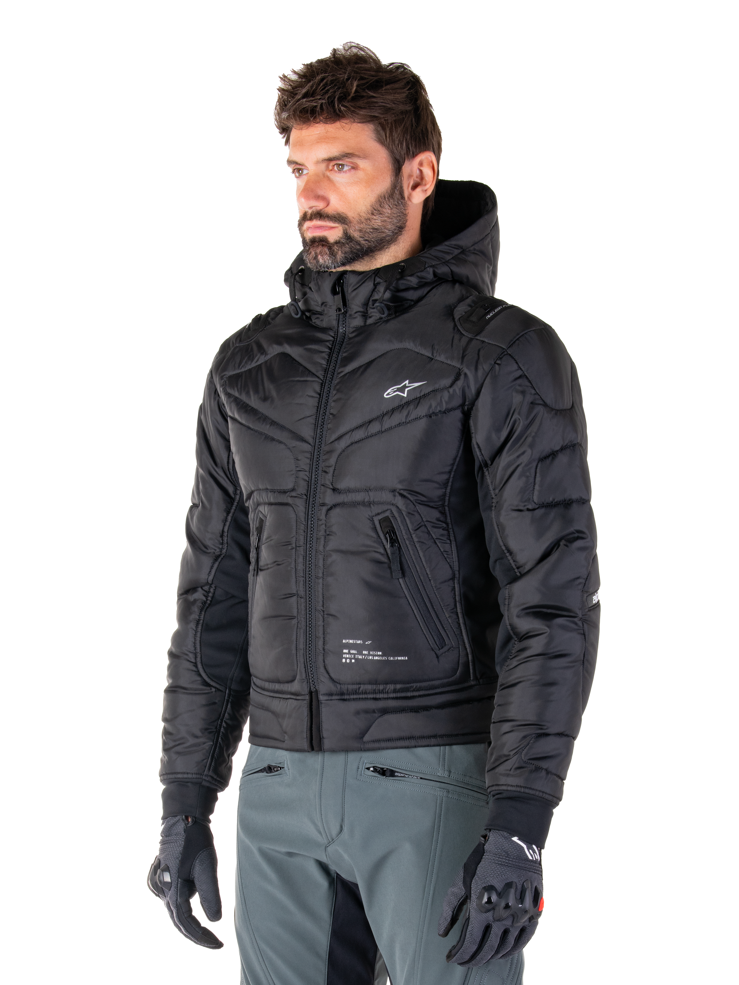 Alpinestars Mohobbs Waterproof Jacket, Black, quilted padded bomber design with a hood, worn by a man with grey riding pants and black gloves, urban streetwear-inspired motorcycle apparel featuring a small white logo on the chest.