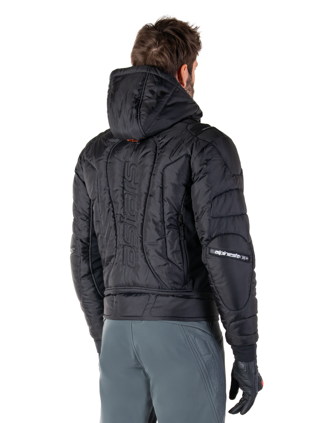 Alpinestars Mohobbs Waterproof Jacket, Black, rear view showing quilted padded construction, hood, vertical astars wordmark on the back, and Alpinestars branding on the sleeves, worn with grey pants and black gloves.