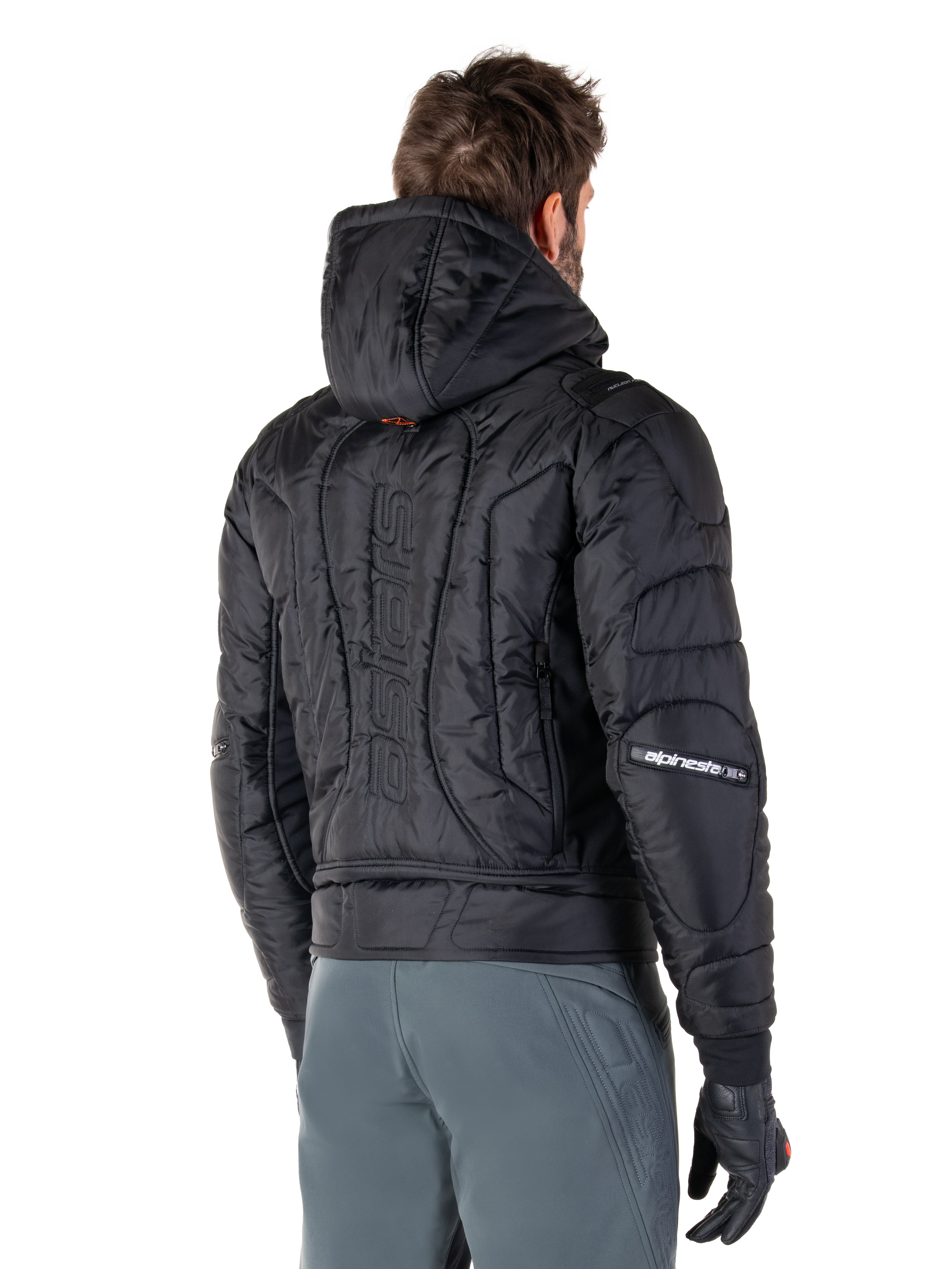 Alpinestars Mohobbs Waterproof Jacket, Black, rear view showing quilted padded construction, hood, vertical astars wordmark on the back, and Alpinestars branding on the sleeves, worn with grey pants and black gloves.