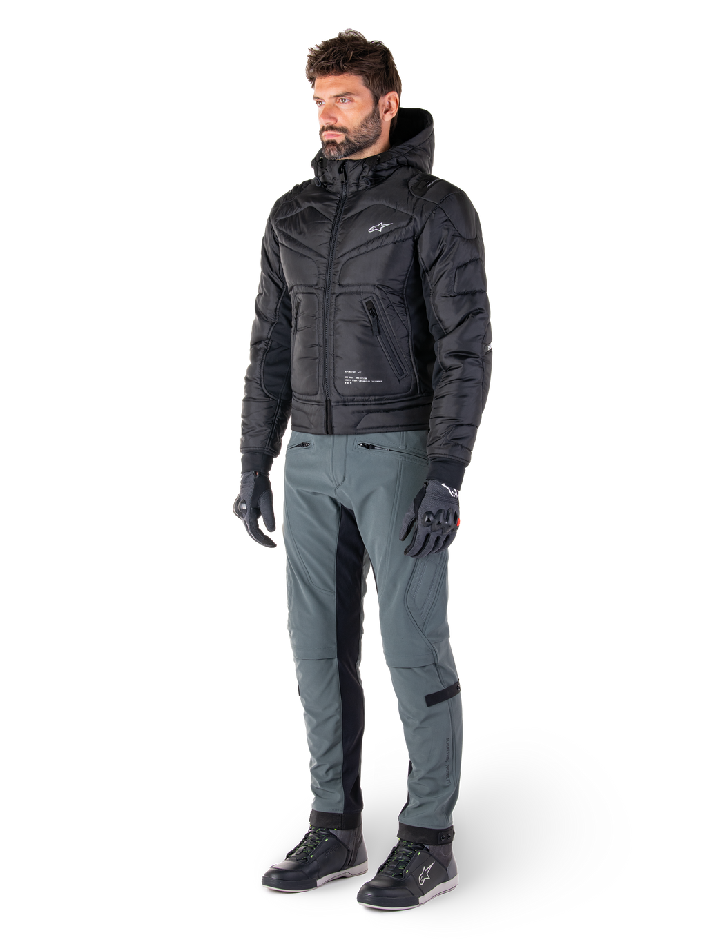 Alpinestars Mohobbs Waterproof Jacket, Black, quilted urban motorcycle bomber jacket with hood, worn by a model with grey riding pants and black gloves, featuring a white chest logo, contemporary streetwear-inspired protective gear