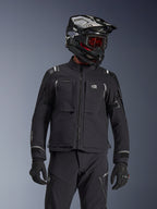 Adventure rider wearing the Alpinestars Andes Pro Drystar® XF Jacket in Black and Dark Gray, featuring All Terra chest branding, paired with matching technical pants and a black adventure helmet with goggles, professional touring gear set.