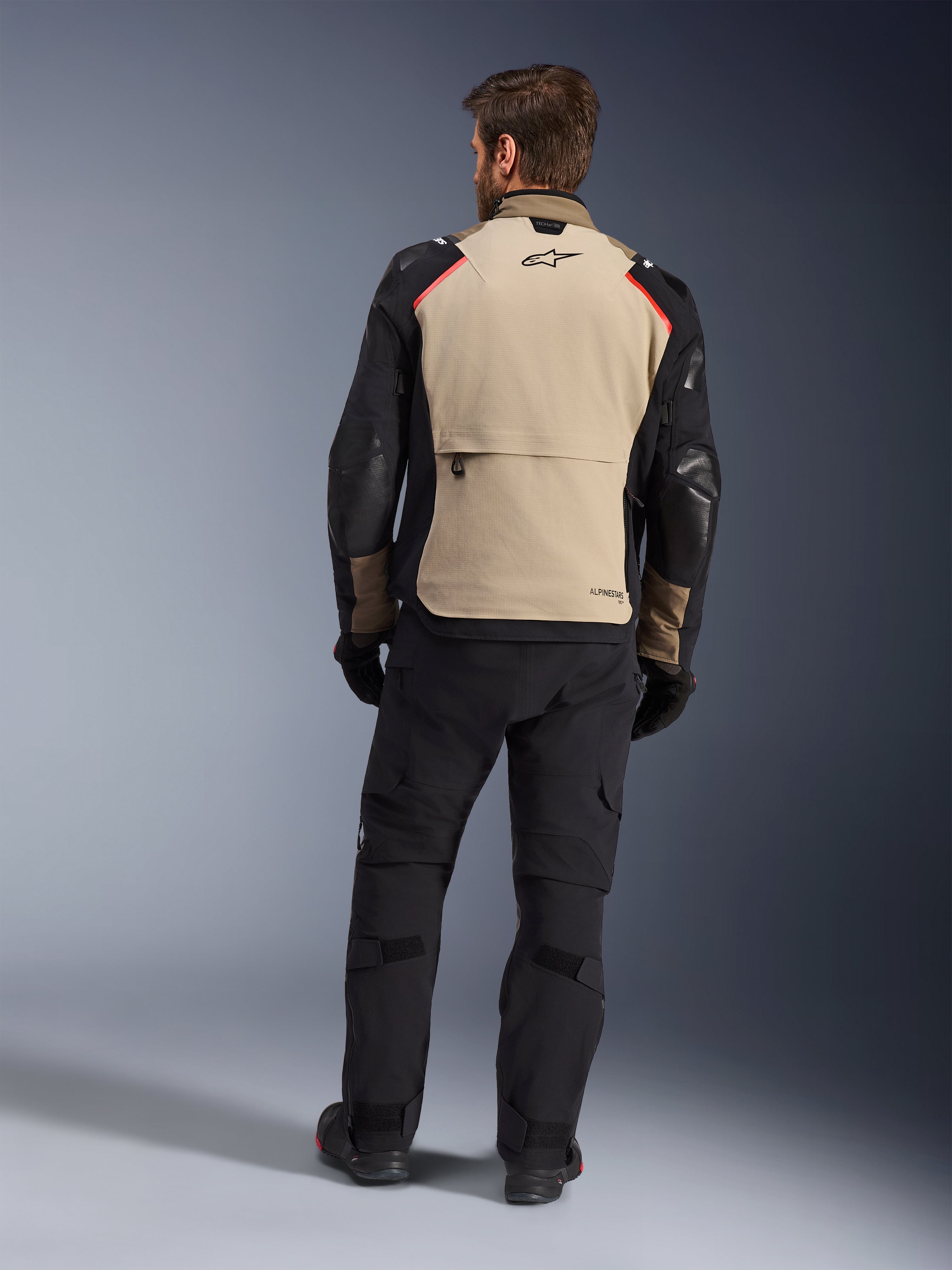 Alpinestars Andes Pro Drystar® XF Jacket, Walnut Aluminum, back view, motorcycle adventure jacket with black sleeves and red shoulder accents, worn with black riding pants and gloves.