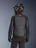 Rider from behind wearing the Alpinestars Cusco Drystar® Jacket in Black and Deep Gray, featuring a large gray back ventilation panel and white logo, paired with a black off-road helmet and black riding gear for adventure touring.