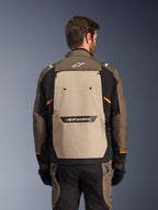Alpinestars Cusco Drystar® Jacket, Walnut Aluminum Black, rear view, featuring a large tan back panel with black logo, orange accents, worn with matching pants and gloves, designed for adventure touring.